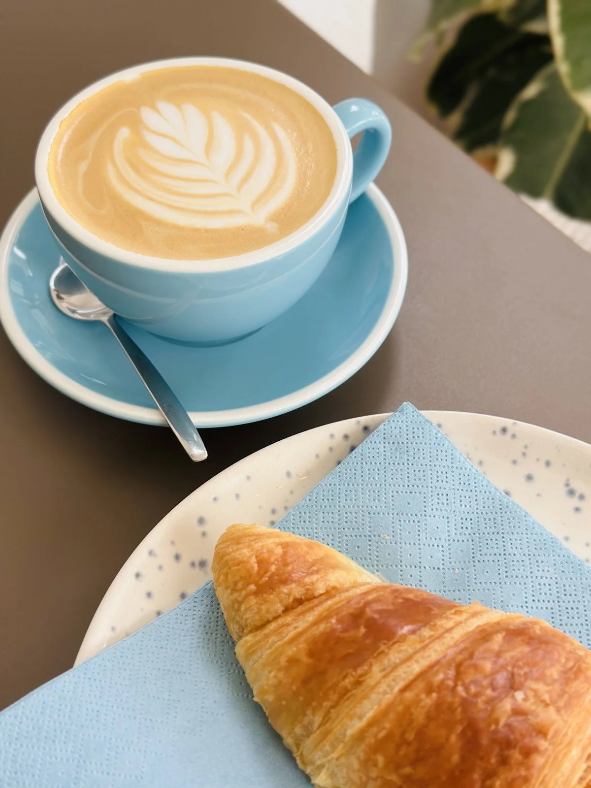 Café com latte art numa chávena azul, acompanhado de um croissant