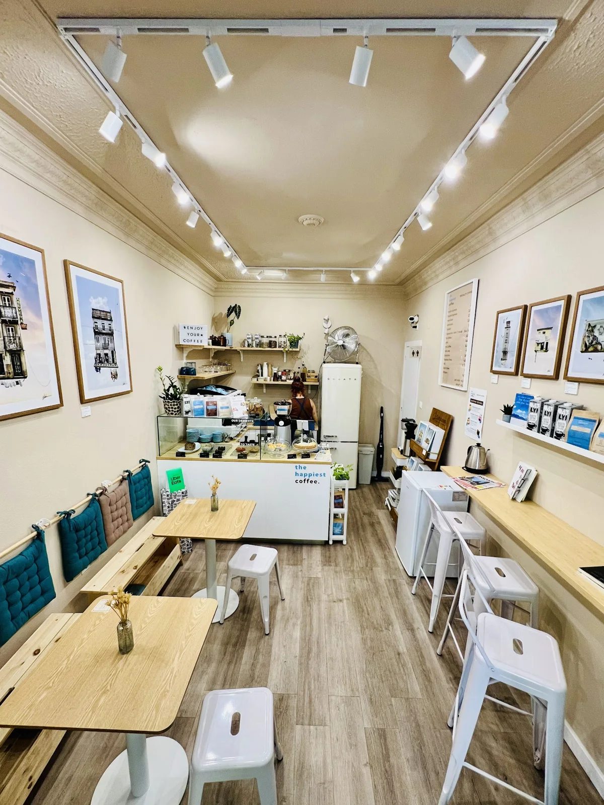 Interior da The Happiest Coffee com mesas de madeira e bancos azuis
